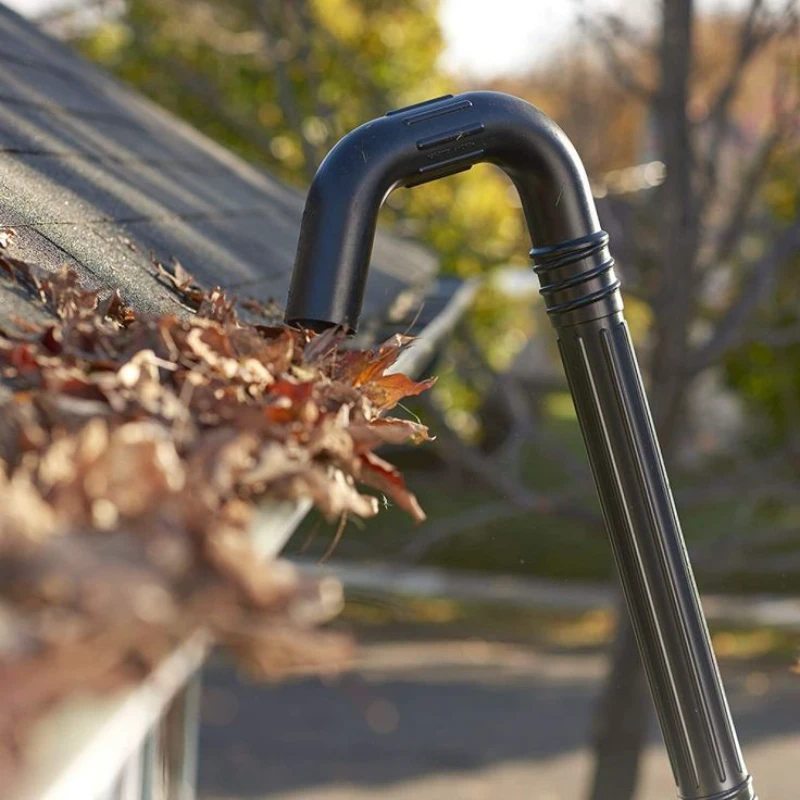 A vacuum tool clearing dry leaves from a roof gutter under clear blue skies, conveying a sense of autumn maintenance and tidiness.