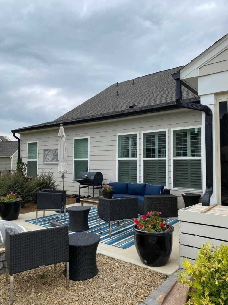 Modern patio with wicker furniture, blue cushions, and striped rug. Large windows overlook the space. Overcast sky adds a calm ambiance.
