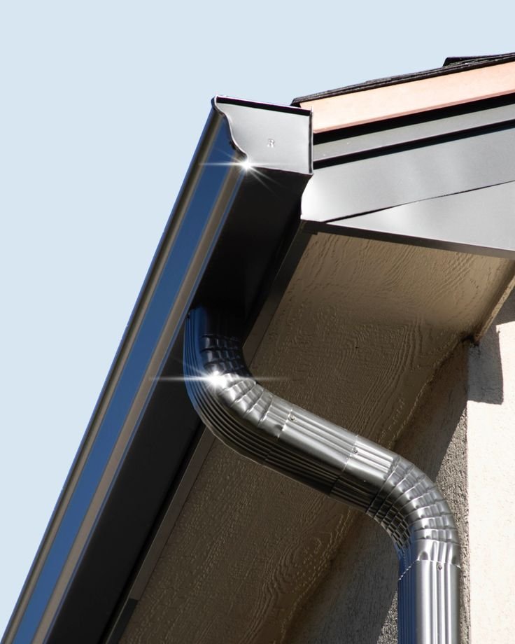 Shiny metallic gutters on a building with blue sky backdrop. The clean, smooth surface reflects sunlight, conveying a sense of newness and precision.