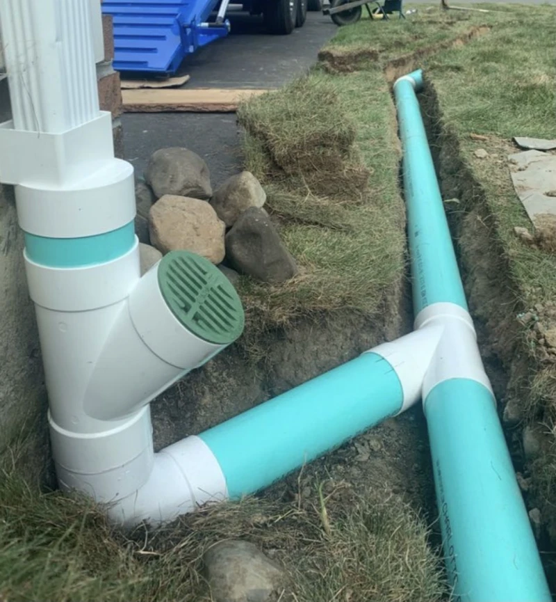 A drainage system with colored PVC pipes installed underground, connected to a downspout.
