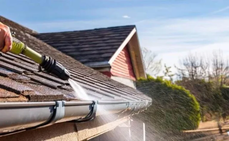 Homeowner pressure washing roof shingles and cleaning gutters to remove dirt, debris, and buildup, helping protect the home's drainage system and prevent water damage. What Is Gutter Cleaning?