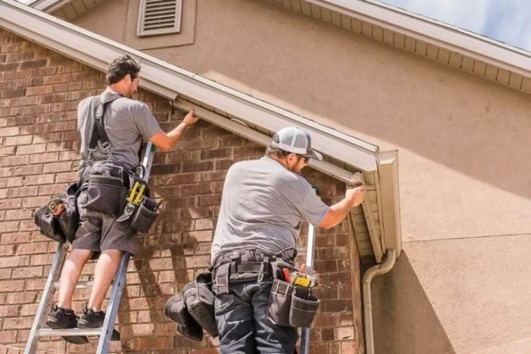 Two workers on ladders performing maintenance on a house's roof and gutters, showcasing professional home improvement services. Gutter Installation Cost in Pittsburgh Explained 2026