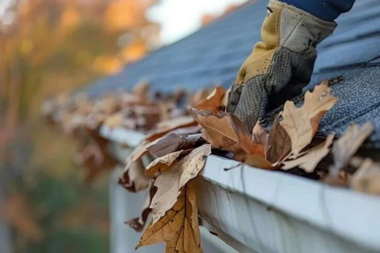 A gloved hand reaches into a gutter filled with fallen autumn leaves. Average Cost of Gutter Cleaning in the Pittsburgh Area?